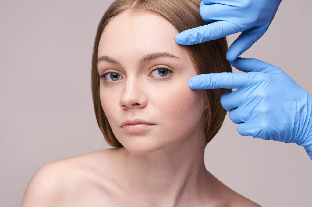 Young woman's face with gloved hands evaluating skin.